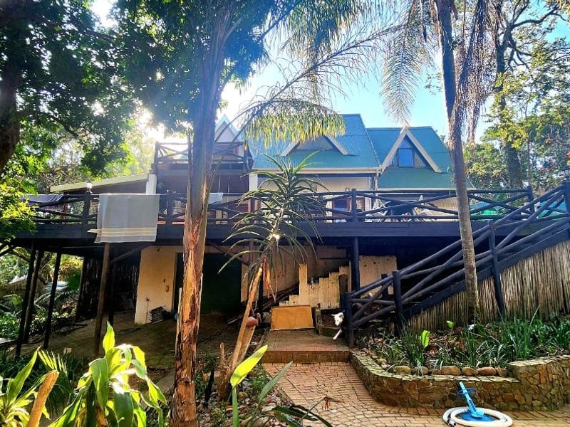 Rear view of the property featuring a large raised timber deck, stone retaining walls, and a lush garden setting.
