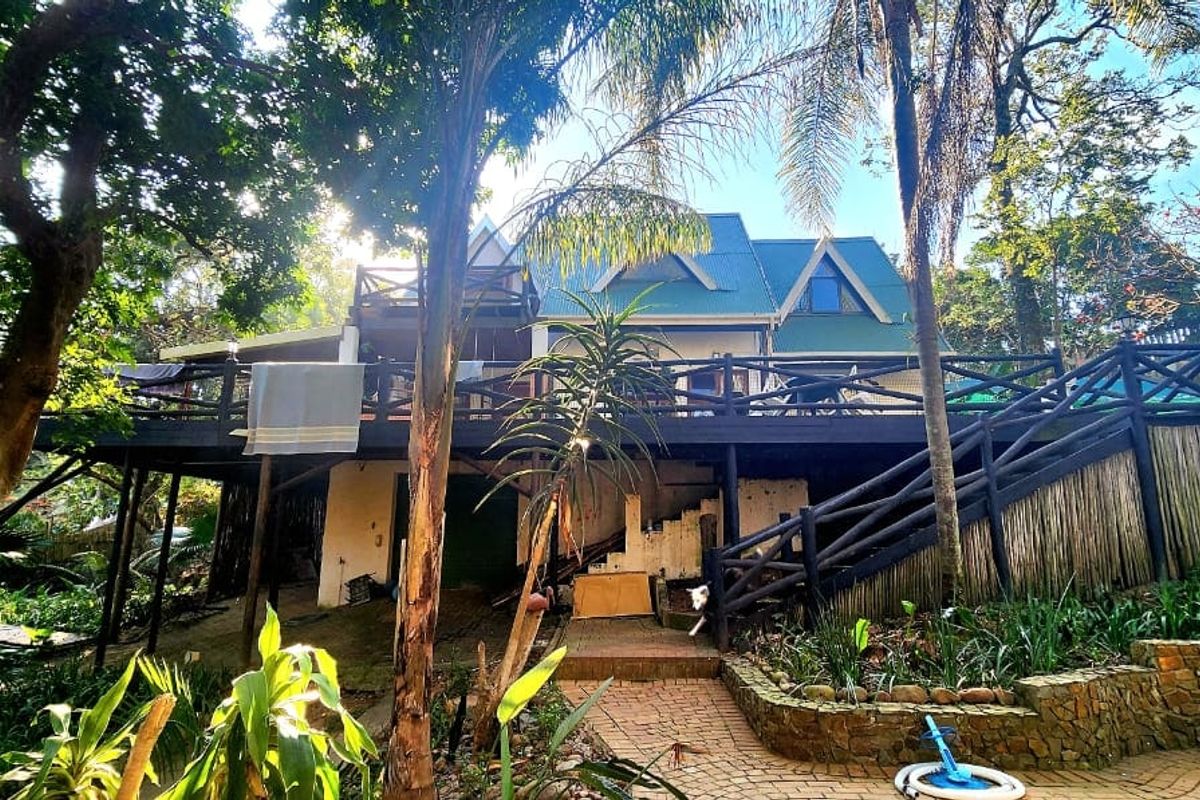 Rear view of the property featuring a large raised timber deck, stone retaining walls, and a lush garden setting.