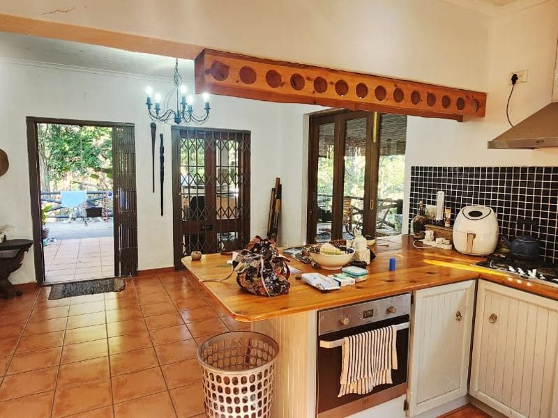 Open-plan kitchen and living area featuring a timber island, built-in oven, extractor fan, and terracotta flooring with direct access to an outdoor patio.