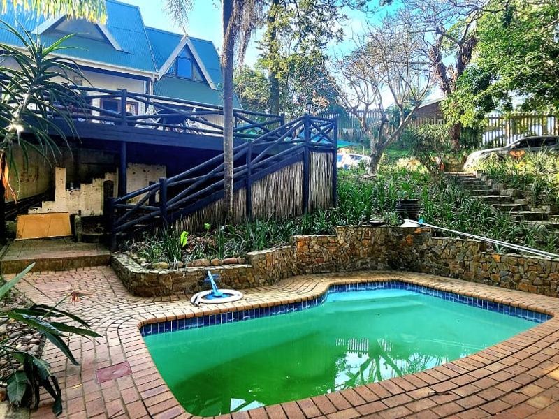 Rear garden area featuring a swimming pool, stone retaining walls, and a raised timber deck with staircase access to the main house.