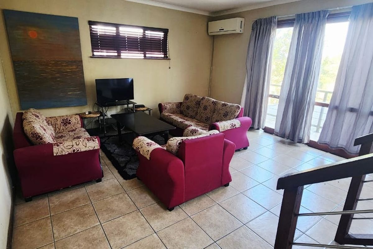 A living room featuring tiled flooring, a split-system air conditioner, and a timber staircase, with sliding glass doors providing access to the exterior.