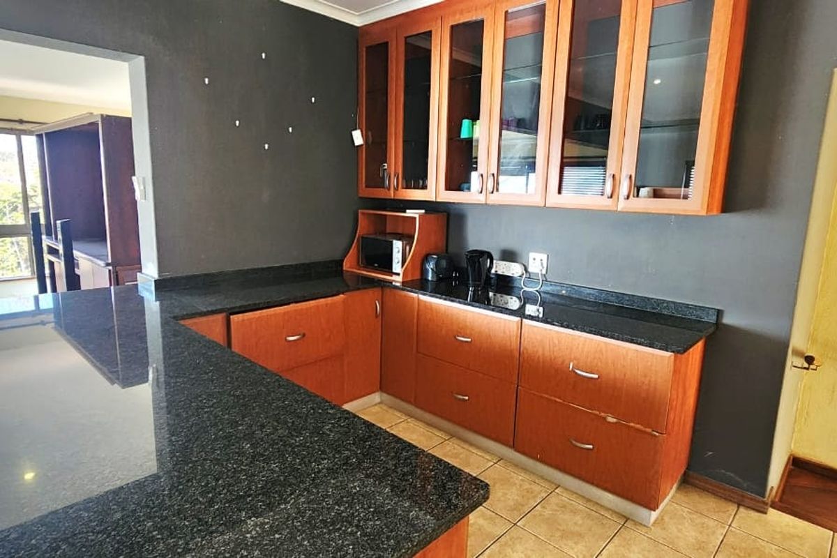 Kitchen featuring wooden cabinetry, granite countertops, and a breakfast bar, with an adjacent view of the living area and staircase.