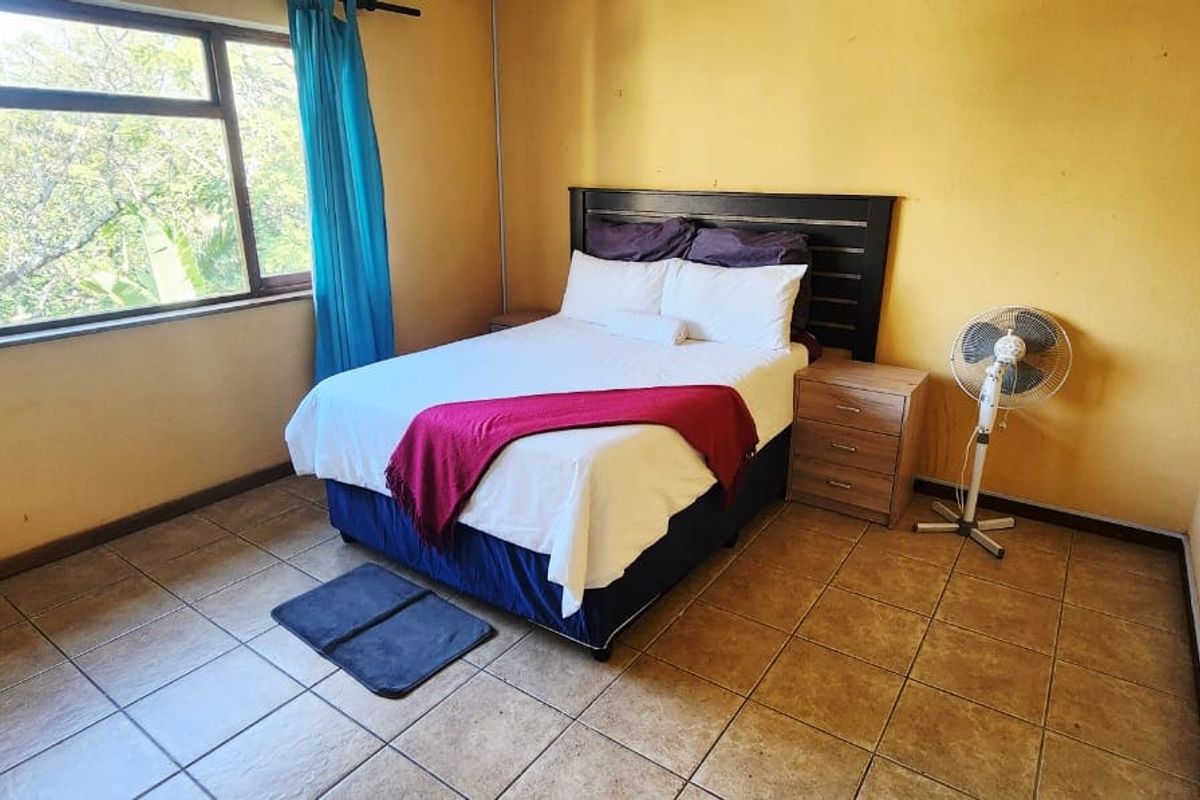 A bedroom featuring tiled flooring and a large window, providing natural light. The space would benefit from a fresh coat of paint.