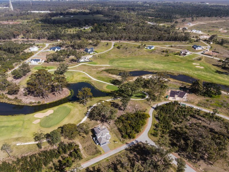 Aerial view of a residential estate featuring golf course fairways, water hazards, and established road infrastructure within a natural landscape.
