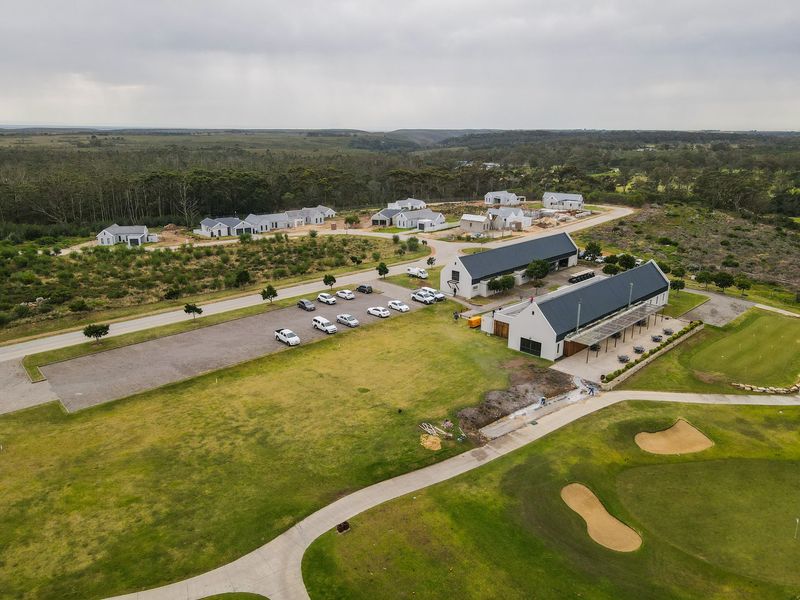 Aerial view of a residential estate development featuring modern pitched-roof buildings, a gravel parking area, and adjacent golf course fairways.
