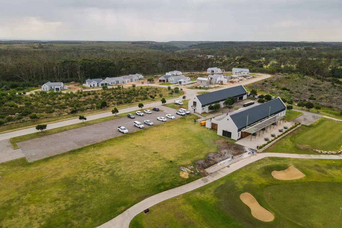 Aerial view of a residential estate development featuring modern pitched-roof buildings, a gravel parking area, and adjacent golf course fairways.