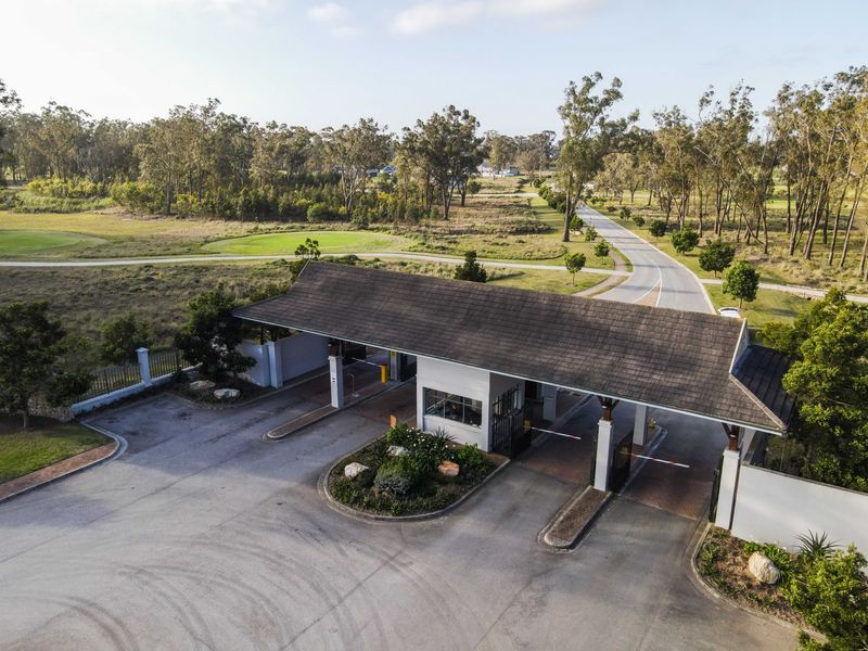 Aerial view of a residential estate security gatehouse featuring boom gates, a tiled roof structure, and landscaped surroundings.