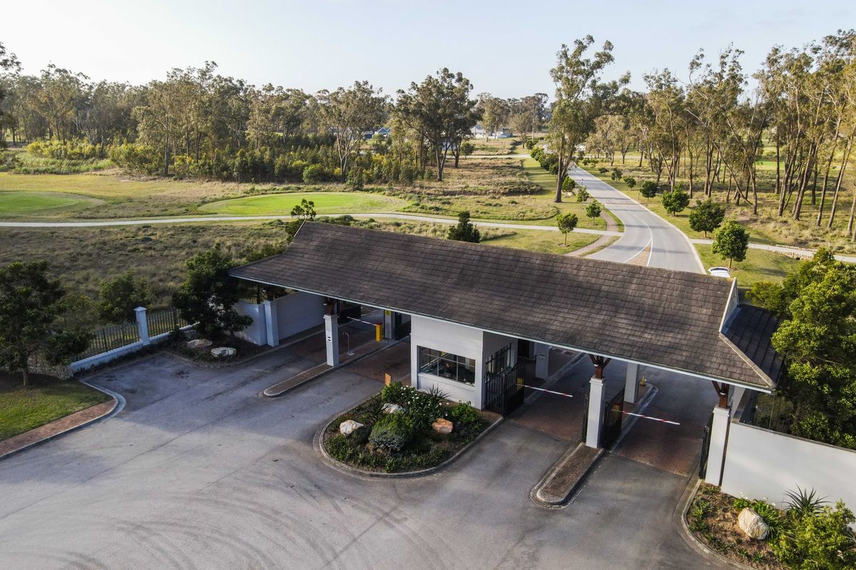 Aerial view of a residential estate security gatehouse featuring boom gates, a tiled roof structure, and landscaped surroundings.