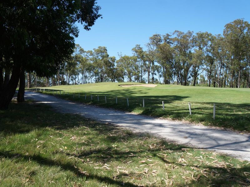 A scenic view of a well-maintained golf course fairway featuring a sand bunker and surrounding mature trees.
