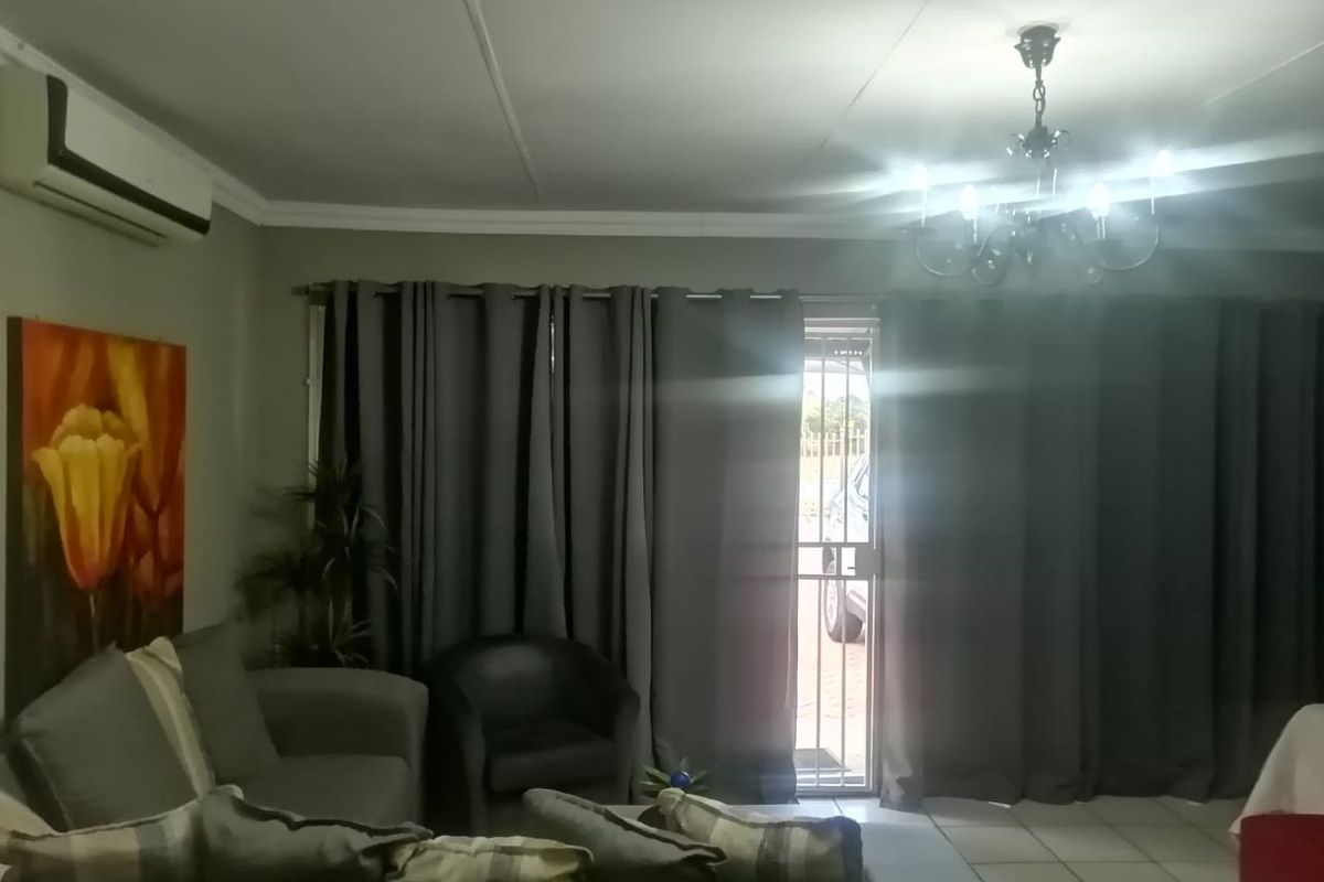 A living room featuring tiled flooring, a split-system air conditioner, and a security gate leading to the exterior.