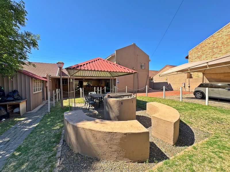 Rear garden area featuring a built-in braai with curved concrete seating, a metal gazebo, and a paved driveway with a carport.