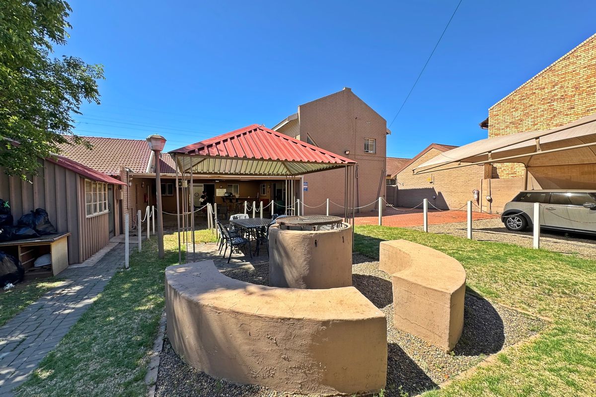 Rear garden area featuring a built-in braai with curved concrete seating, a metal gazebo, and a paved driveway with a carport.
