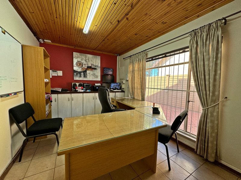 A functional home office featuring tiled flooring, built-in cabinetry, and a timber tongue and groove ceiling with large window and security bars.