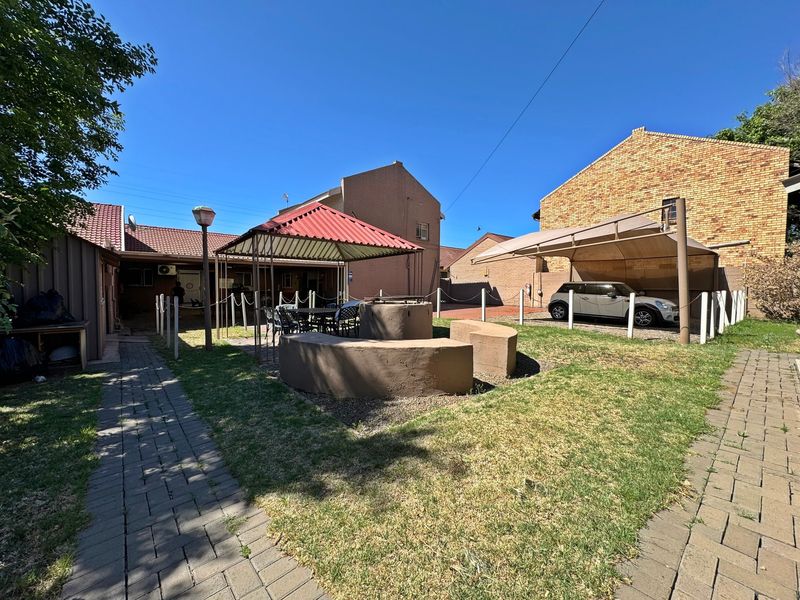 Rear garden area featuring a paved walkway, built-in braai, gazebo, and a covered carport structure.