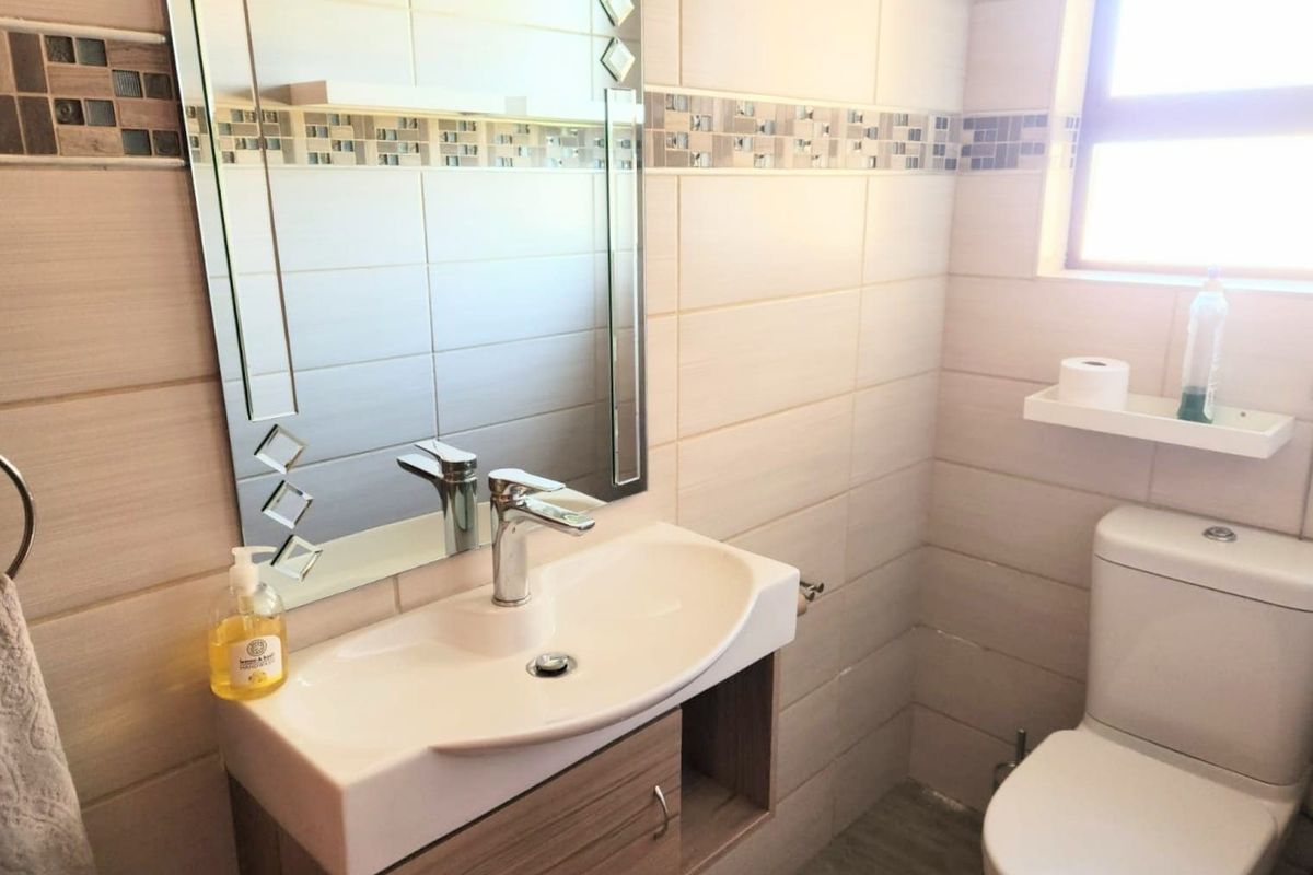 A modern bathroom featuring a vanity cabinet with a ceramic basin, chrome mixer tap, decorative wall-mounted mirror, and neutral ceramic tiling with mosaic accents.