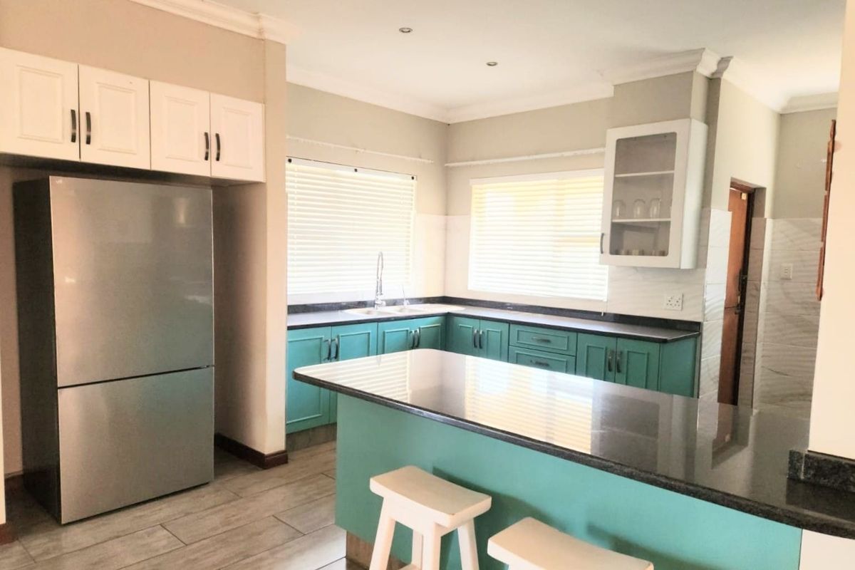 A well-lit kitchen featuring teal cabinetry, granite countertops, a central island, and tiled flooring, offering a functional and modern workspace.