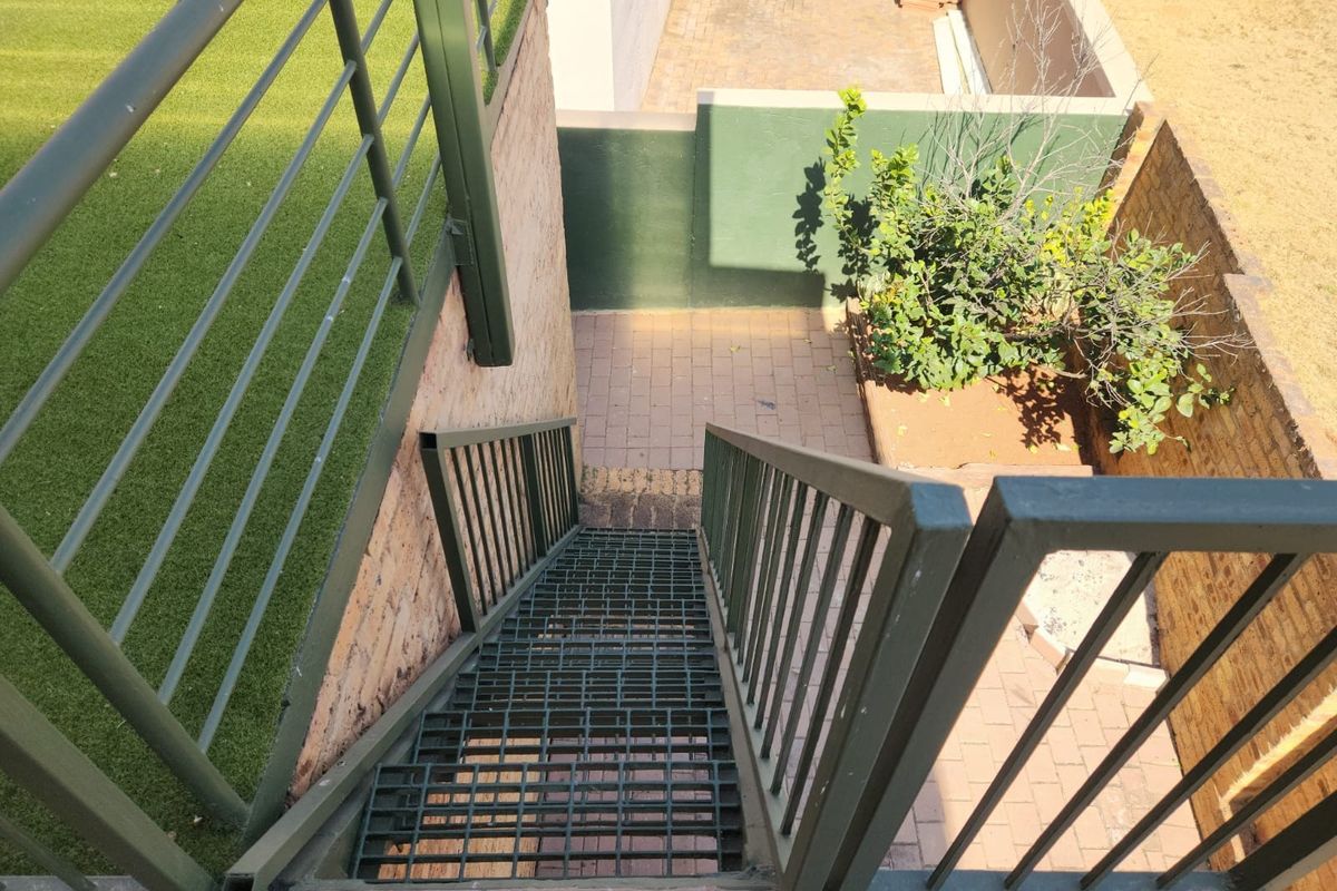 An elevated view of a metal staircase leading down to a paved rear courtyard area with retaining walls and artificial turf.