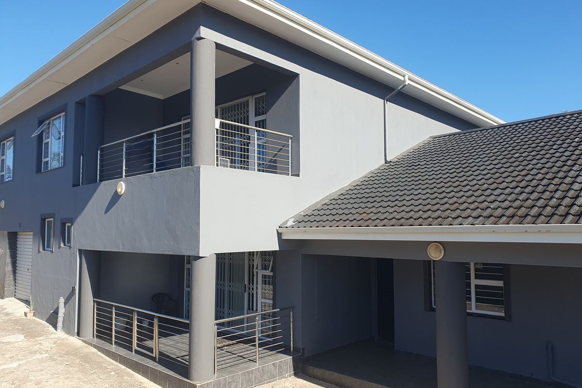 A modern double-story exterior view featuring a tiled roof, covered patio, and upper-level balcony with stainless steel railings and security gates.