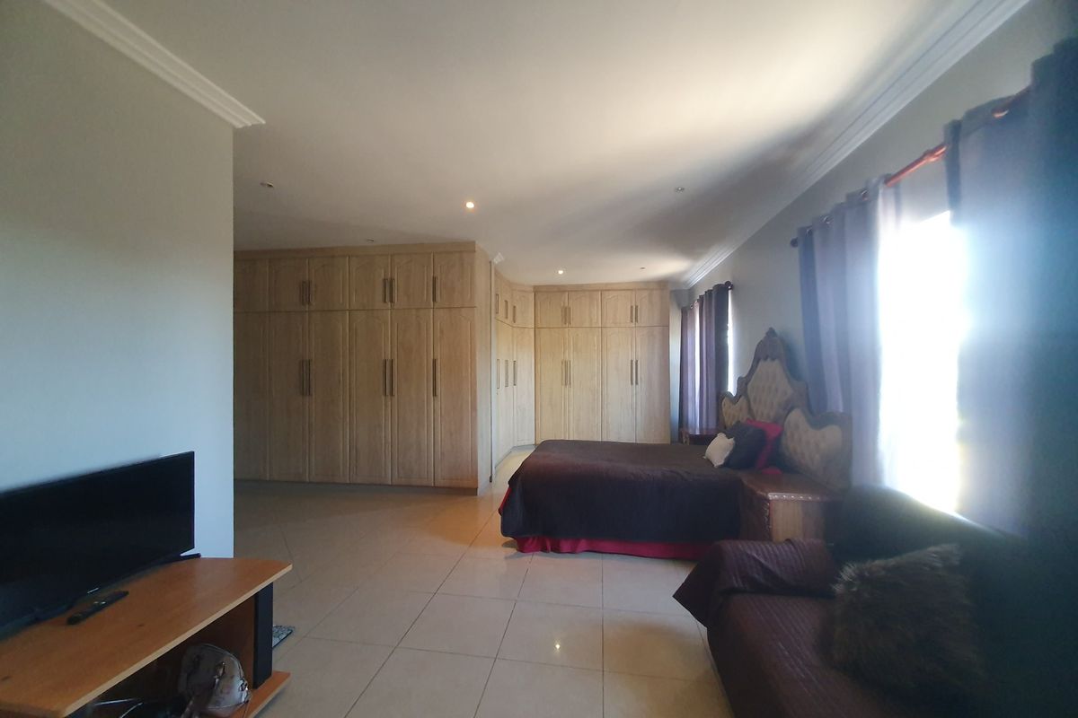 Spacious bedroom featuring extensive built-in wooden cupboards, tiled flooring, and recessed downlighting.