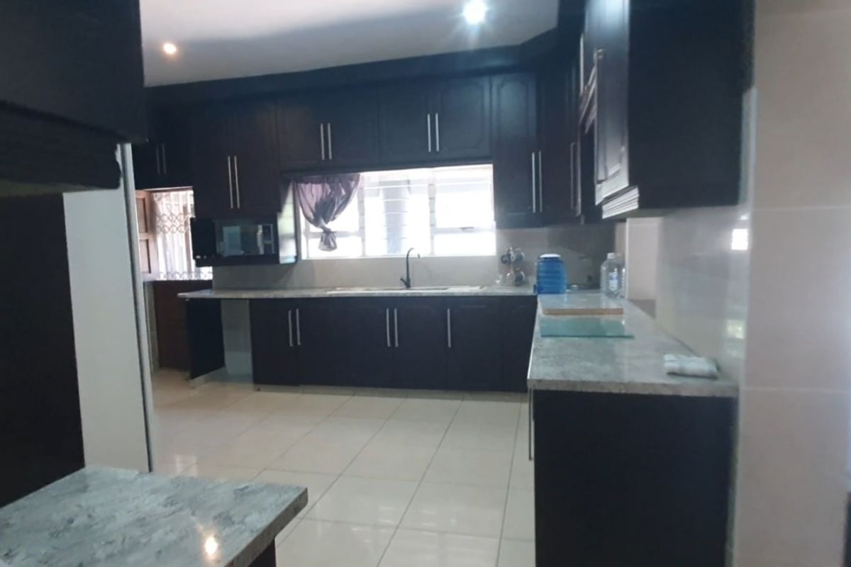 A spacious kitchen featuring dark wood cabinetry, granite countertops, and tiled flooring, offering a clean and functional layout for culinary activities.