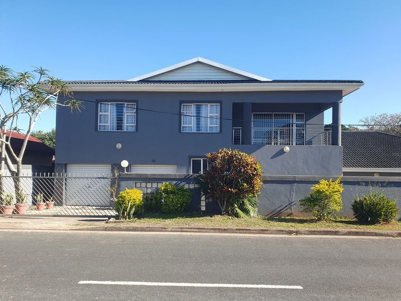 Front elevation of a double-story house featuring a double garage, a balcony with security gates, and a well-maintained perimeter wall.