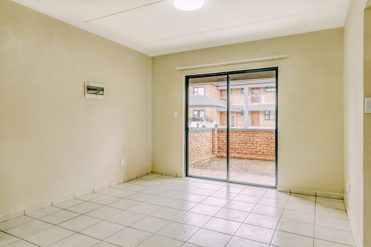 An empty living room featuring ceramic floor tiles and a sliding glass door providing access to an outdoor patio area.
