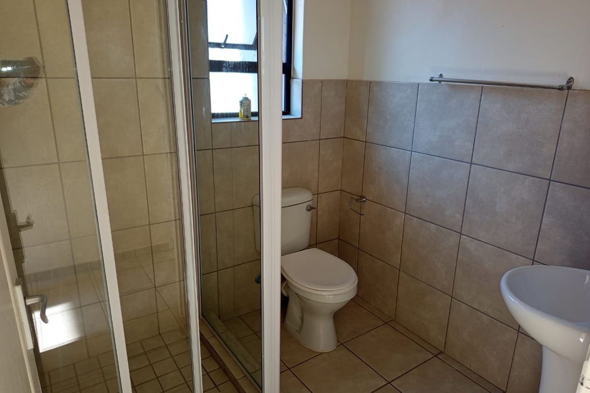 A functional bathroom featuring a shower enclosure, pedestal basin, and toilet with neutral wall and floor tiling.