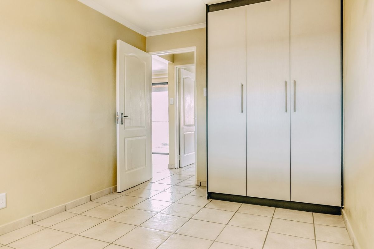 A bright, empty bedroom featuring neutral wall tones, tiled flooring, and a large built-in wardrobe with modern handles.