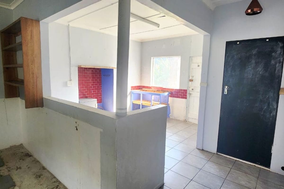 An empty kitchen area featuring tiled flooring, built-in shelving, and a tiled splashback, requiring cosmetic updates and finishing touches.