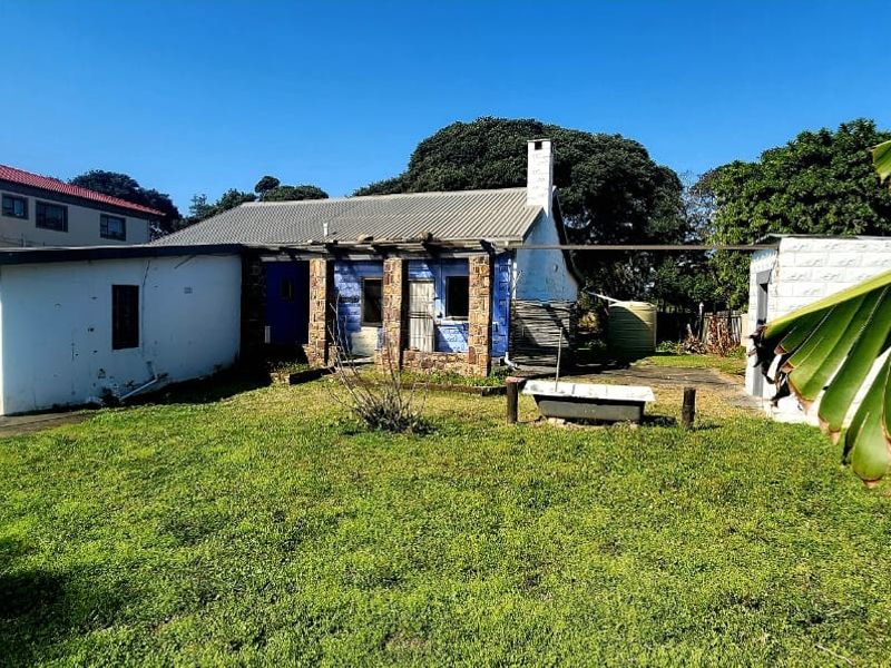Rear view of the property featuring a stone-clad facade, corrugated metal roofing, and a spacious backyard area with a water tank.