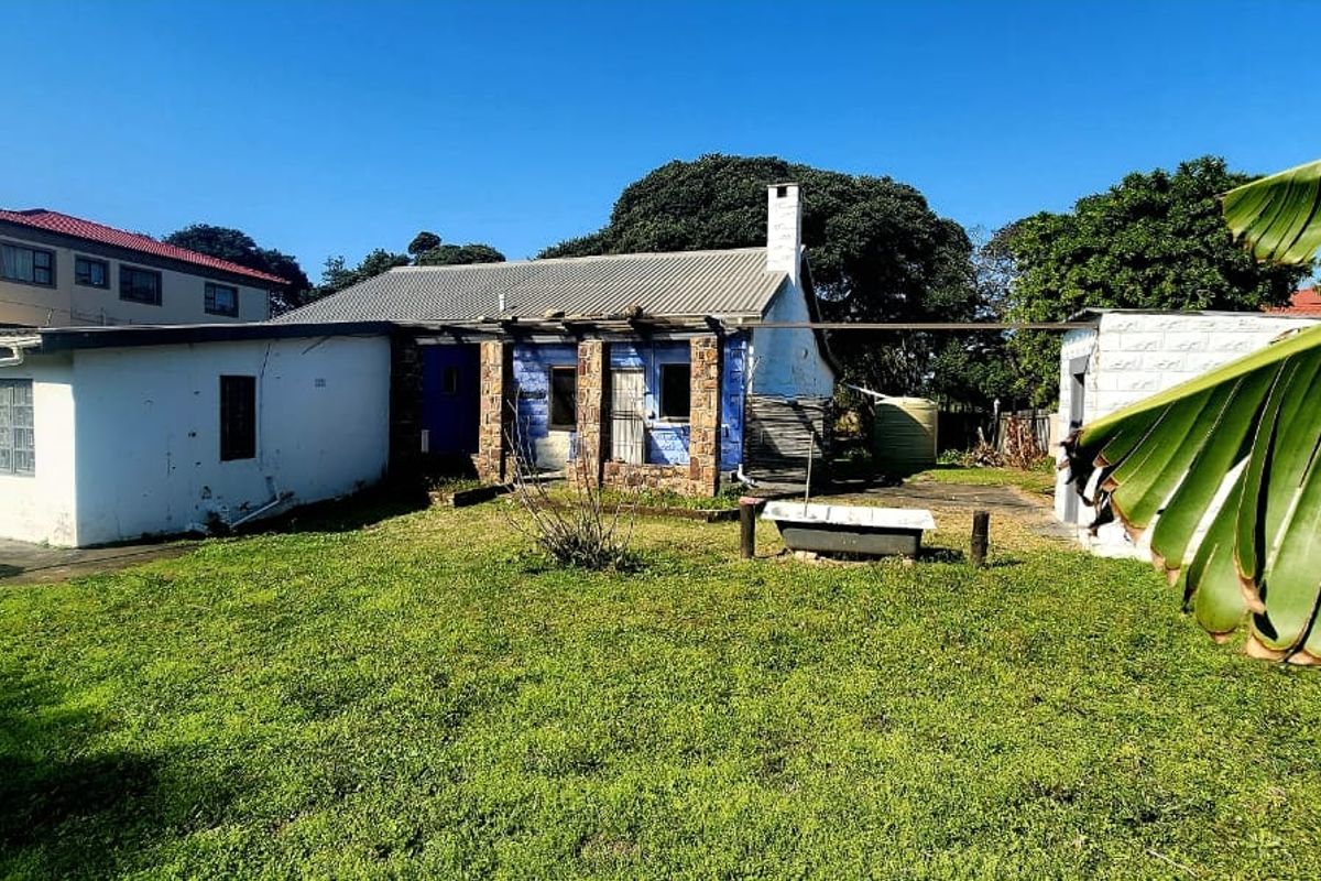 Rear view of the property featuring a stone-clad facade, corrugated metal roofing, and a spacious backyard area with a water tank.