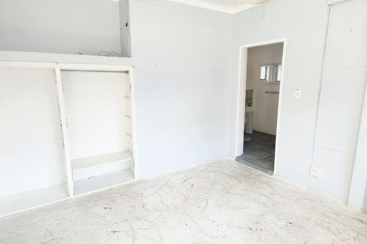 An empty bedroom featuring a built-in wardrobe, an arched entryway, and an adjacent staircase, requiring cosmetic updates to the flooring and wall finishes.