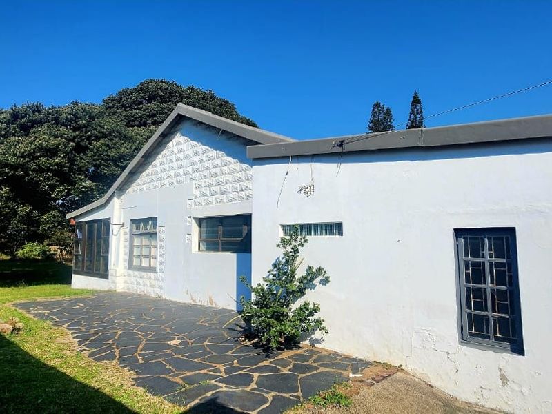 Rear view of the property featuring a stone-paved patio area, steel-framed windows, and a gable roof structure set against a garden backdrop.