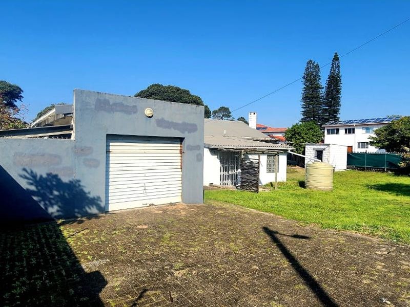 Rear exterior view featuring a detached garage with a roller shutter door, paved driveway, and a spacious garden area with a water storage tank.
