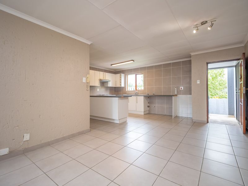 Open-plan living and kitchen area featuring neutral tiled flooring, built-in cabinetry, and direct access to an outdoor balcony.