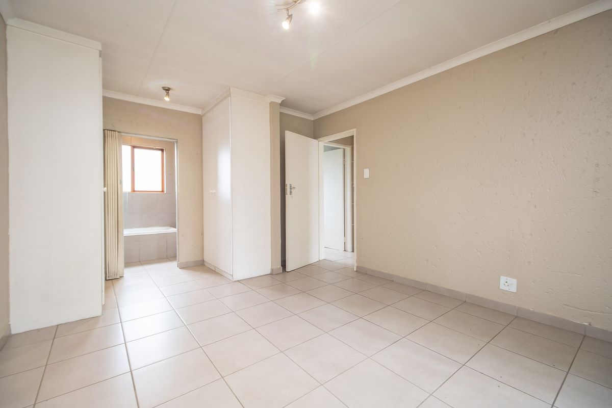 An empty bedroom featuring tiled flooring, built-in cupboards, and neutral wall finishes, with an adjoining bathroom visible through the doorway.