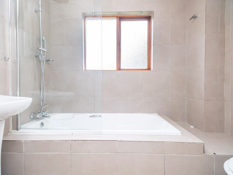 A functional bathroom featuring a built-in bathtub with a glass shower screen, pedestal basin, and neutral wall tiling.