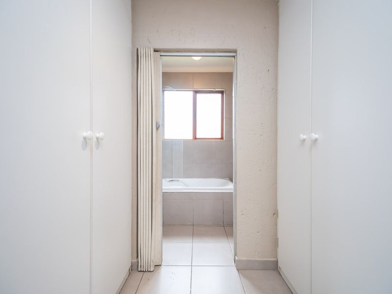 A hallway featuring built-in cupboards leading into a bathroom with a tiled bathtub and neutral finishes.