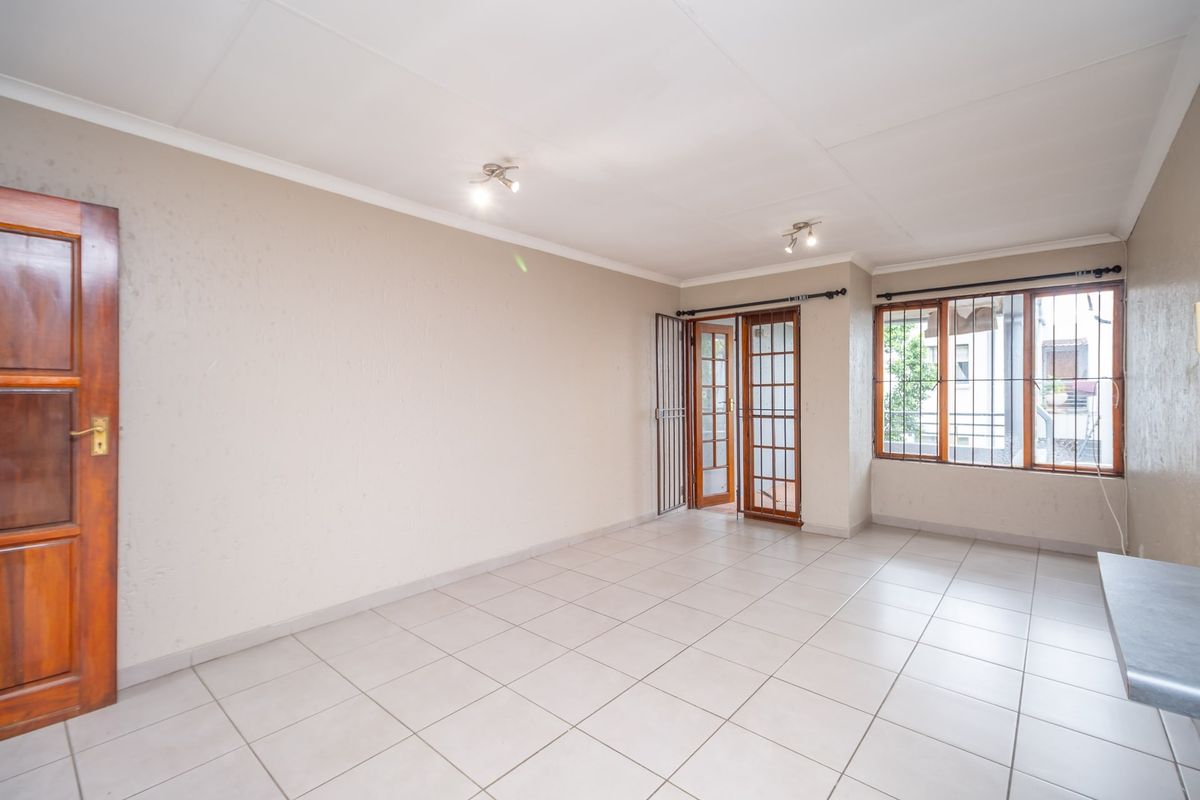 A bright, empty living area featuring neutral tiled flooring, wooden door access, and large windows with security bars, offering a clean canvas for styling.