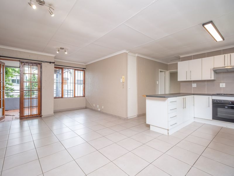 An open-plan living and kitchen area featuring tiled floors, modern white cabinetry, built-in oven, and direct access to a balcony through a security gate.