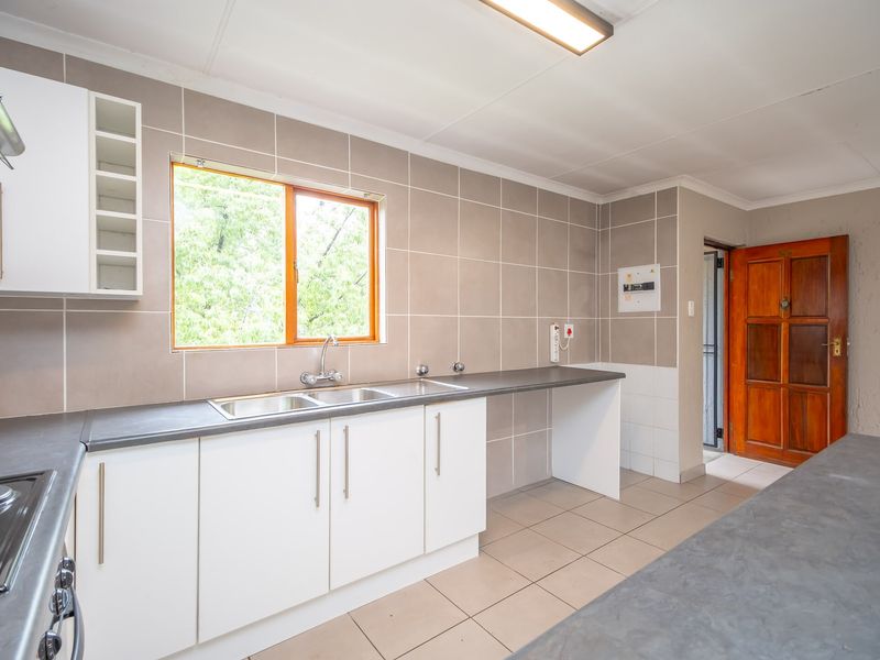 A clean, functional kitchen featuring white cabinetry, grey laminate countertops, ceramic wall tiles, and a built-in hob with an extractor fan.