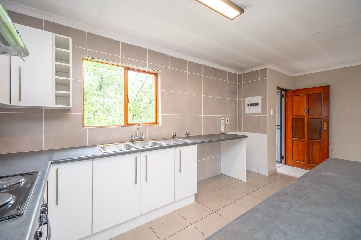 A clean, functional kitchen featuring white cabinetry, grey laminate countertops, ceramic wall tiles, and a built-in hob with an extractor fan.