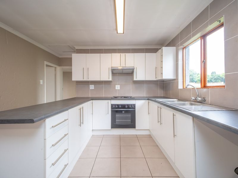 A clean, functional kitchen featuring white cabinetry, dark laminate countertops, built-in oven with hob, and tiled flooring.