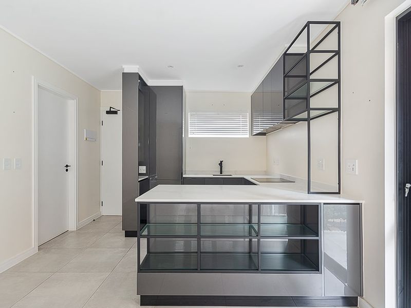 Modern kitchen featuring sleek grey cabinetry, stone countertops, integrated shelving, and neutral tile flooring, offering a clean and contemporary aesthetic.