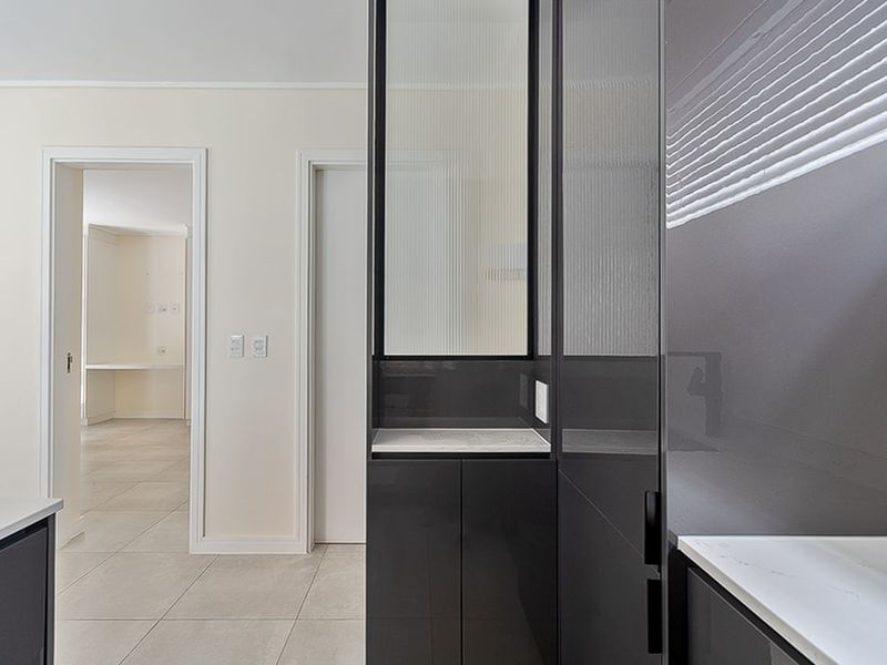 Modern kitchen area featuring sleek dark cabinetry, stone countertops, and a decorative fluted glass partition, leading into an adjacent room.