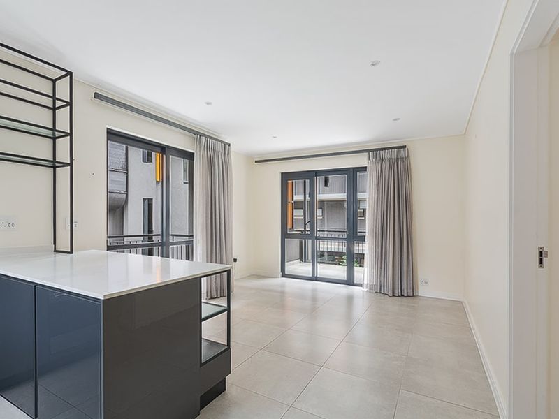 Bright open-plan living area featuring a modern kitchen island with stone countertop, tiled flooring, and large sliding glass doors leading to a balcony.