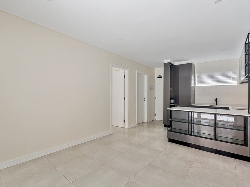 An open-plan living and kitchen area featuring modern cabinetry, a kitchen island, tiled flooring, and recessed lighting in a clean, vacant space.