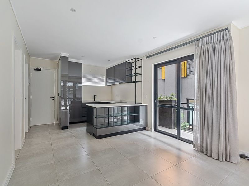 Modern open-plan kitchen and living area featuring sleek cabinetry, a central island, tiled flooring, and direct access to a private balcony.