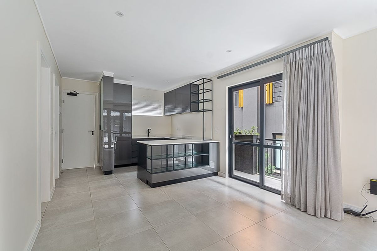 Modern open-plan kitchen and living area featuring sleek cabinetry, a central island, tiled flooring, and direct access to a private balcony.