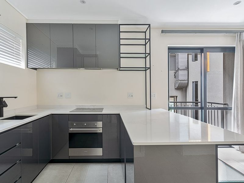 Modern kitchen featuring sleek grey gloss cabinetry, stone countertops, integrated oven and hob, and direct access to a private balcony.